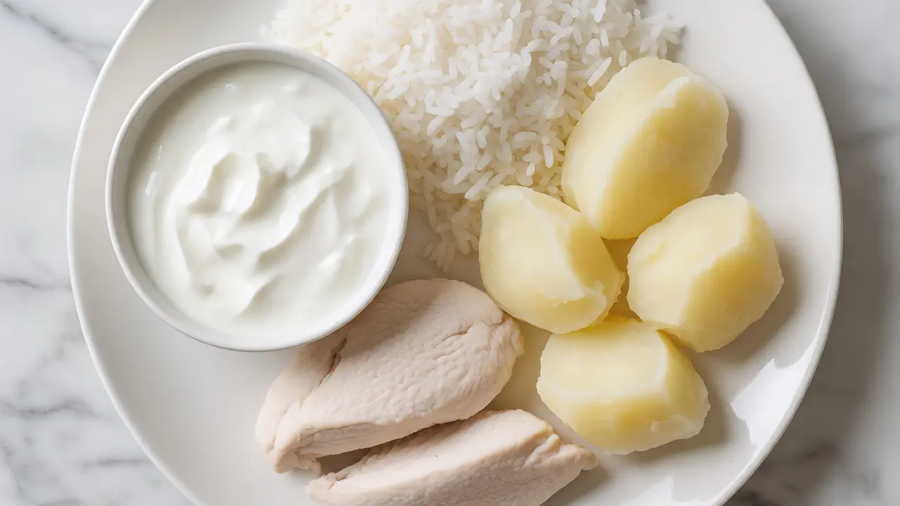 Jídla bílé diety: kuře, rýže, brambory a jogurt na bílém talíři.